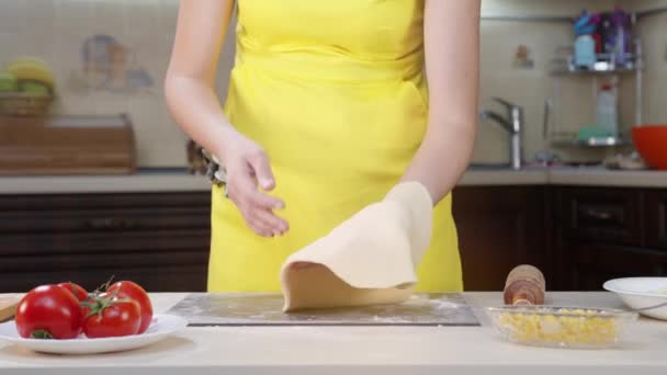 La cocinera arroja masa en sus manos. Preparación de masa de pizza. Mujer con ropa amarilla y tomates en la mesa . — Vídeo de stock