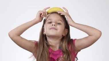 Küçük kız beyaz arka planda muzla oynaşıyor. Kafasında muz olan bir kızın komik duyguları..
