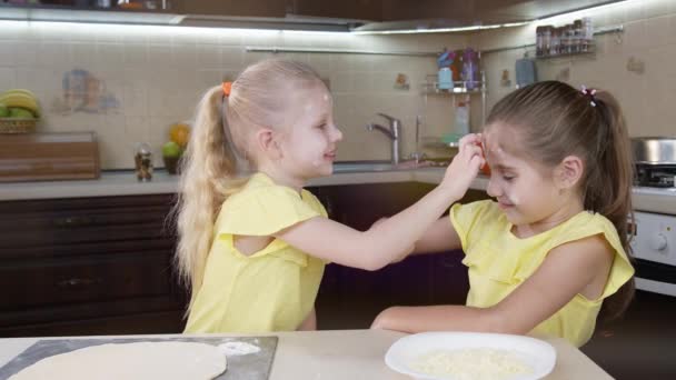 As crianças brincam com farinha na cozinha. Duas meninas felizes pagam seus rostos em dor um ao outro . — Vídeo de Stock