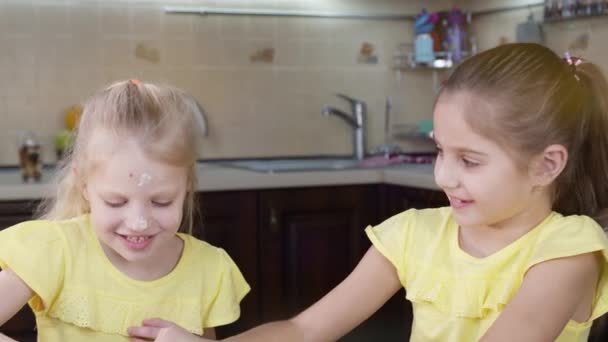 As crianças brincam com farinha na cozinha. Duas meninas felizes pagam seus rostos em dor um ao outro . — Vídeo de Stock