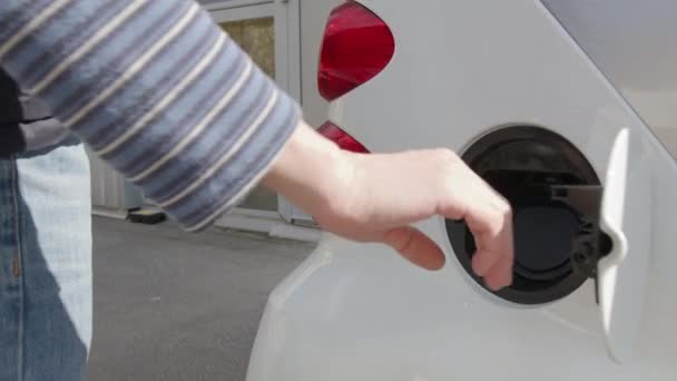 Mans χέρι εισάγει το καλώδιο φόρτισης για να φορτίσετε το ηλεκτρικό αυτοκίνητο. Φόρτιση ηλεκτρικού αυτοκινήτου σε βενζινάδικο. — Αρχείο Βίντεο