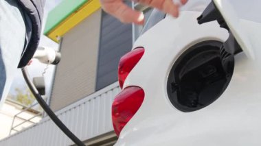 İnsanlar elektrikli arabayı şarj etmek için kabloyu yerleştirirler. Benzin istasyonunda elektrikli araba şarj etmek..