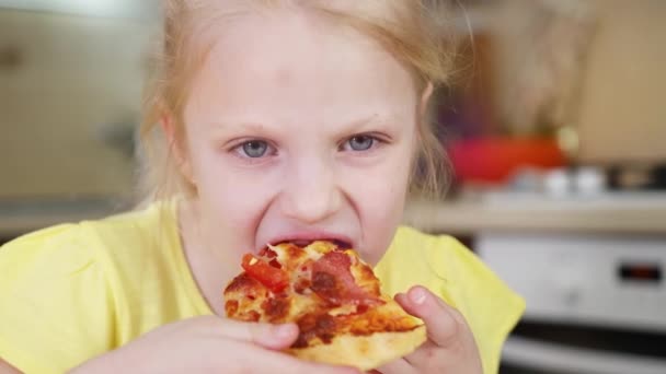 La bambina morde una fetta di pizza da vicino e mangia deliziosamente la pizza. La ragazza appetitosamente mastica la pizza . — Video Stock