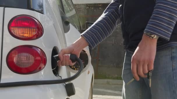 Mans main insère le câble de charge pour charger la voiture électrique. Chargement d'une voiture électrique dans une station-service . — Video