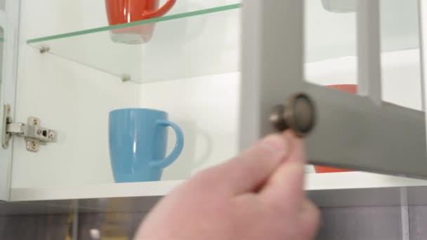 In Großaufnahme einer Männerhand öffnet sich ein Küchentisch mit bunten Tassen. Farbige Tassen in der Küche hinter dem Glas. — Stockvideo