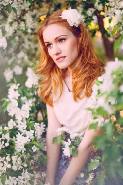 Çiçek açan elma ağacında poz veren kızıl saçlı bir model..