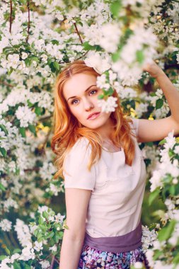 Çiçek açan elma ağacında poz veren kızıl saçlı bir model..