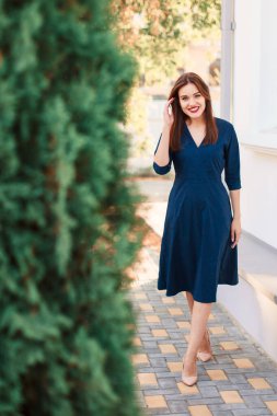 Bahçede poz veren koyu mavi elbiseli kızıl saçlı bir manken..