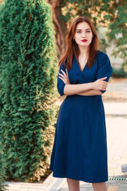 Bahçede poz veren koyu mavi elbiseli kızıl saçlı bir manken..