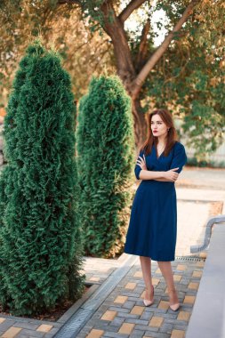 Bahçede poz veren koyu mavi elbiseli kızıl saçlı bir manken..