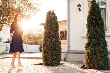 Kızıl saçlı manken gün batımında bahçede poz veriyor.