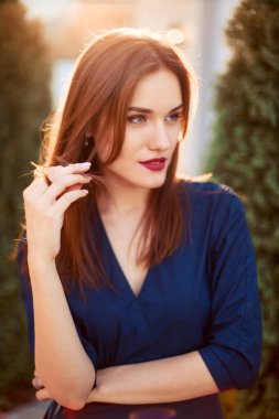 Bahçede poz veren koyu mavi elbiseli kızıl saçlı bir manken..