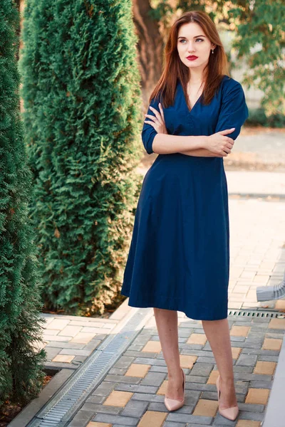 Bahçede poz veren koyu mavi elbiseli kızıl saçlı bir manken..