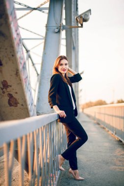 Pantolon ve ceketle köprüde poz veren bir model..