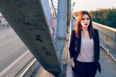 Pantolon ve ceketle köprüde poz veren bir model..