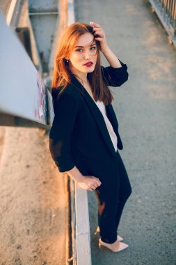 Pantolon ve ceketle köprüde poz veren bir model..