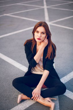 Takım elbiseli kızıl saçlı manken yazın bir otoparkta oturur.