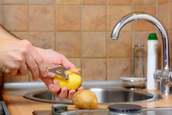 Descascando uma batata com descascador em uma cozinha — Fotografia de Stock