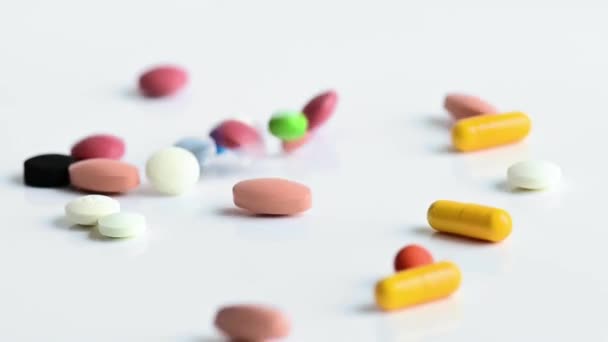 Pílulas médicas coloridas, cápsulas e comprimidos que caem sobre a mesa branca — Vídeo de Stock