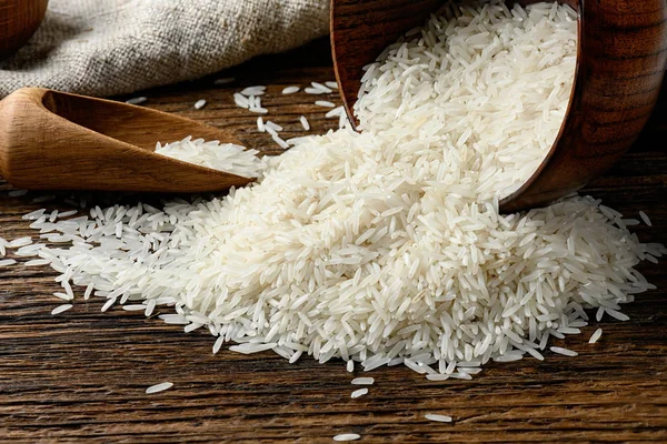 Montón de arroz largo sin cocer derramado del tazón sobre una mesa de madera . —  Fotos de Stock