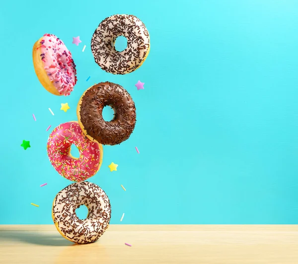 Fliegende Donuts. Mischung aus bunten süßen Krapfen mit Streusel auf türkisblauem Hintergrund, der auf den Tisch fällt. — Stockfoto