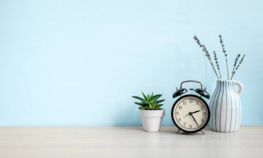 Boş mavi duvar ve masa, alarm saati, ev bitkisi ve seramik vazo. Boşluğu kopyala