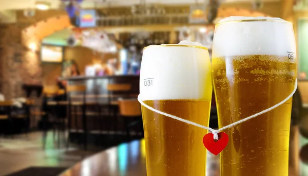Dois copos de cerveja para os amantes com coração vermelho. Pub interior fundo . — Fotografia de Stock