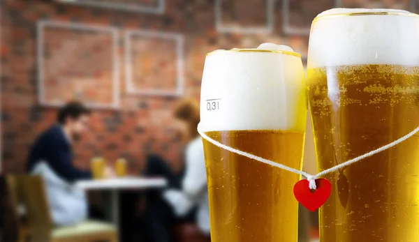 Dois copos de cerveja para os amantes com coração vermelho. Pub interior casal desfrutando de bebida no fundo — Fotografia de Stock