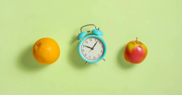 오렌지와 애플은 건강 한 식사와 가벼운 녹색 배경의 알람 시계를 위한 과일을 생산 한다. 위에서 본 모습. 편평 한 침대. — 스톡 사진
