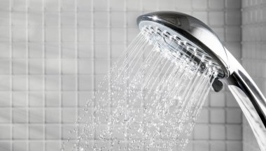 Shower head with running water in white bathroom clipart