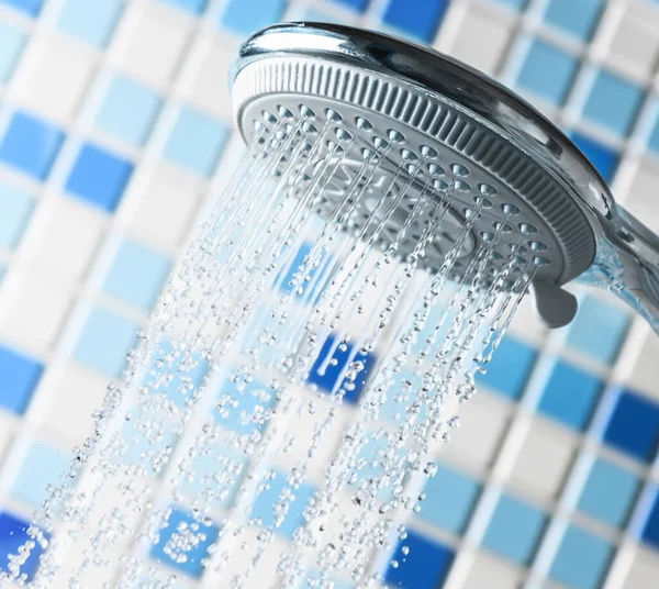 Shower head with flowing water stream in blue bathroom close-up. — Stock Photo, Image