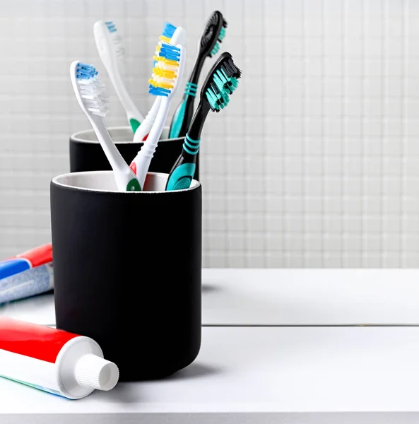 Toothbrushes in a black glass and toothpaste in front of a mirror on the bathroom close up. — Stock Photo, Image