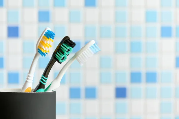 Toothbrushes close-up in a black glass on the blue mosaic tile wall background. Copy space — Stock Photo, Image