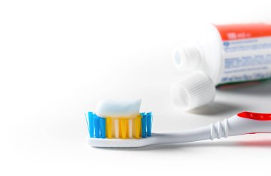 Toothbrush with toothpaste and tube of toothpaste over white background