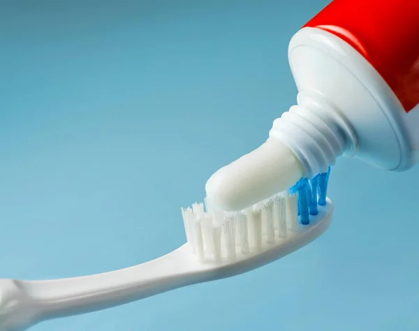 Squeezing toothpaste from tube onto toothbrush close up on blue background — Stock Photo, Image