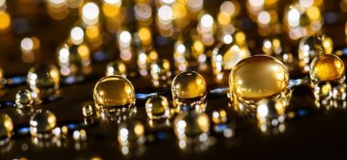 Gold shiny background with droplets, on black surface. Golden sparkle particles macro. Luxury abstract background.