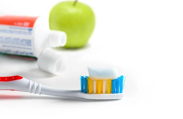 Toothbrush with squeezed paste, tube of toothpaste and green apple on white background. Selective focus. — Stock Photo, Image