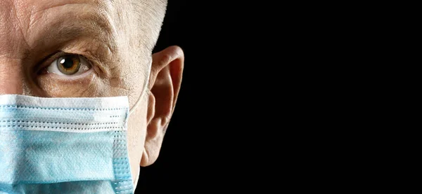 Man in medical mask looking at camera on black background close-up. Copy space