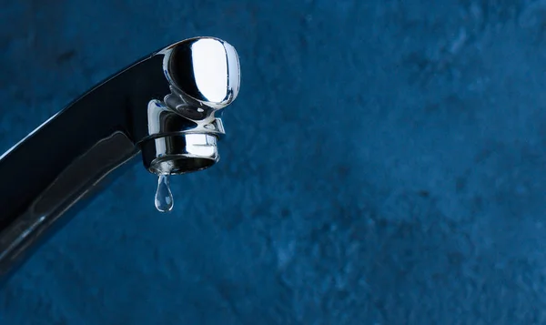 Torneira e gota de água close-up no fundo azul. Conceito de consumo de água — Fotografia de Stock