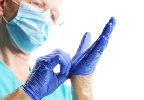 Lekarz w masce medycznej zakłada niebieskie rękawiczki odizolowane na biało — Zdjęcie stockowe