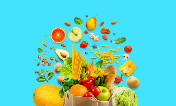 Sortimento de comida saudável no saco de compras e em torno dele. Legumes e frutas, mantimentos sobre fundo azul aqua . — Fotografia de Stock