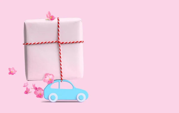 Coche azul con caja de regalo en el techo y flores sobre fondo rosa. Copiar espacio . —  Fotos de Stock