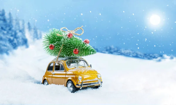 雪の冬の森の屋根の上にクリスマスツリーを運ぶレトロなおもちゃの車。クリスマスの背景。休日カード。スペースのコピー. — ストック写真