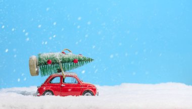 Kırmızı oyuncak araba, mavi arka plandaki karda çatıda Noel ağacı taşıyor. Noel arkaplanı. Tatil kartı. Boşluğu kopyala.