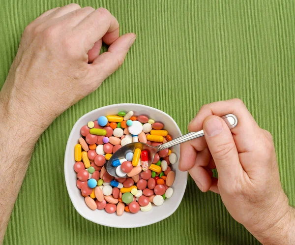A pessoa come um monte de comprimidos, comprimidos, cápsulas de uma tigela com uma colher na mesa de jantar. Vista superior . — Fotografia de Stock