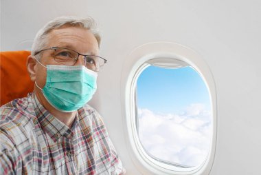 Uçak kabininde maskeli bir adam, bulutlu bir uçak penceresi. Coronavirus COVID-19 salgını sırasında önleme