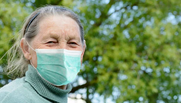 Portret uśmiechniętej starszej kobiety w masce medycznej na zewnątrz wioski. Zapobieganie podczas pandemii koronawirusowej COVID-19 — Zdjęcie stockowe