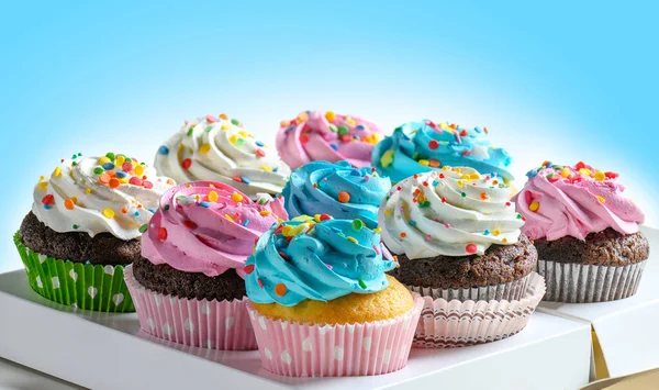宅配ボックスでおいしいカップケーキパッケージ、ピンクの白と青のクリームと青の背景にカラフルなスプリンクルを持つ様々なカップケーキ — ストック写真