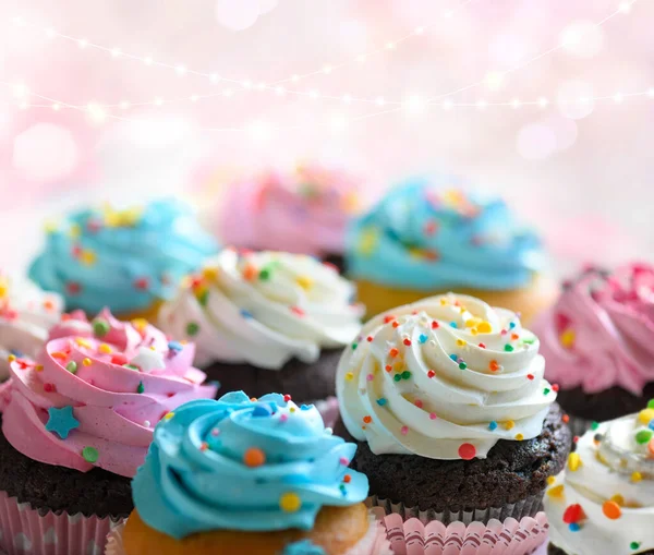 Cupcakes com creme rosa branco e azul e polvilhas coloridas sobre fundo rosa com luzes bokeh. Foco seletivo, DOF superficial . — Fotografia de Stock
