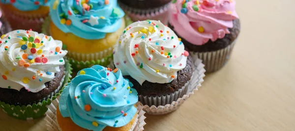 Cupcakes com creme branco e azul rosa e polvilhas coloridas na mesa . — Fotografia de Stock
